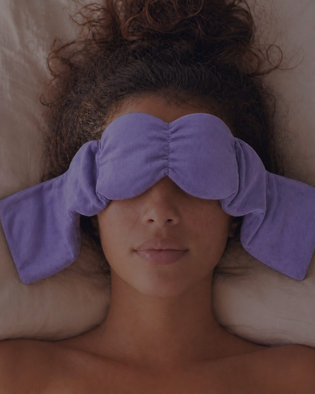Dreamery plush weighted eye mask in a low-light bedroom for darker, calmer nights.